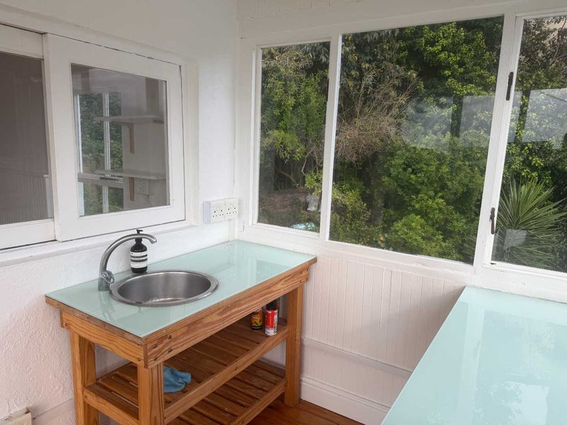 A bright scullery or utility area featuring a stainless steel sink, glass-topped wooden cabinetry, and large windows overlooking a garden.