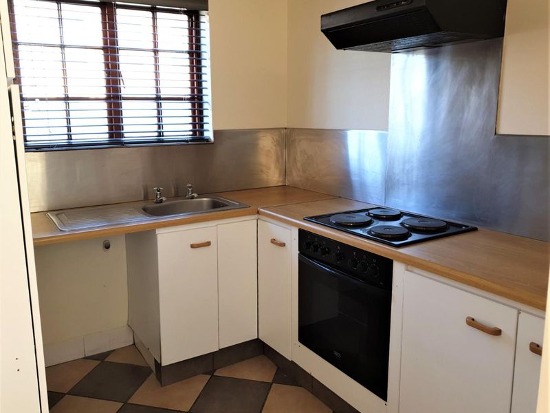 A functional kitchen featuring built-in cabinetry, a stainless steel splashback, integrated oven and hob, and tiled flooring.