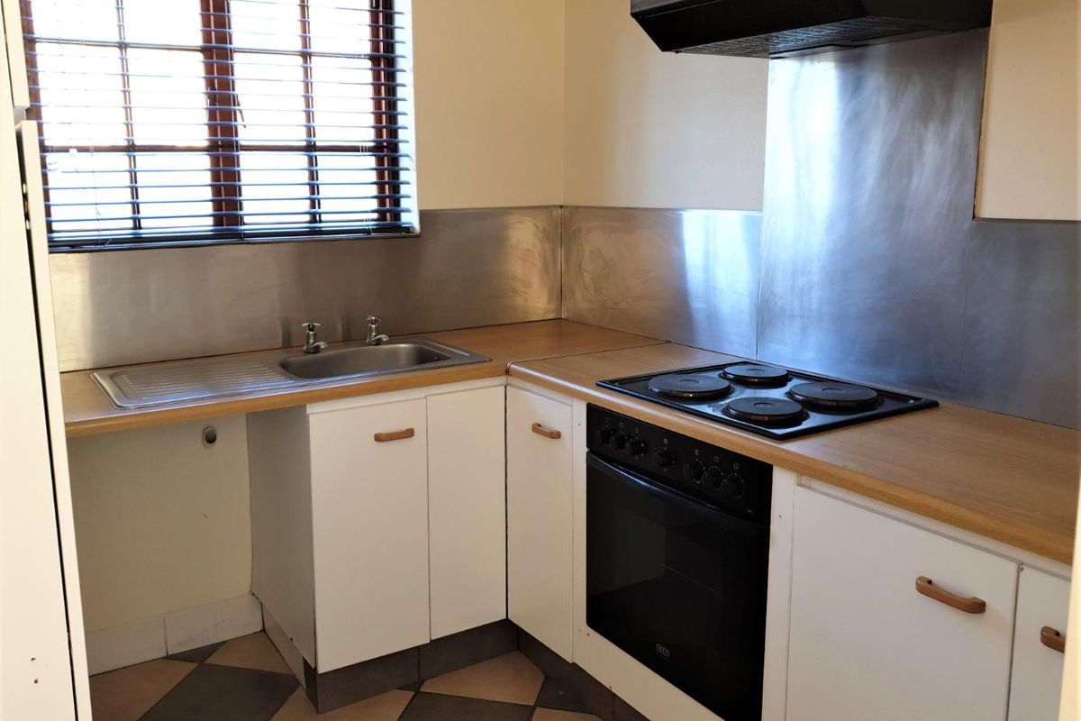 A functional kitchen featuring built-in cabinetry, a stainless steel splashback, integrated oven and hob, and tiled flooring.