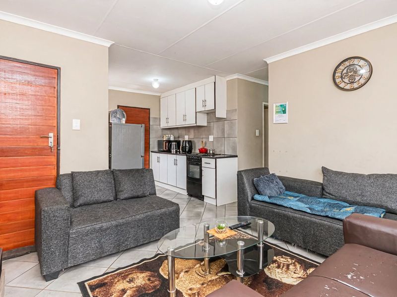 Open-plan living area featuring tiled flooring and a compact kitchen with built-in cabinetry, tiled backsplash, and integrated stove and oven.