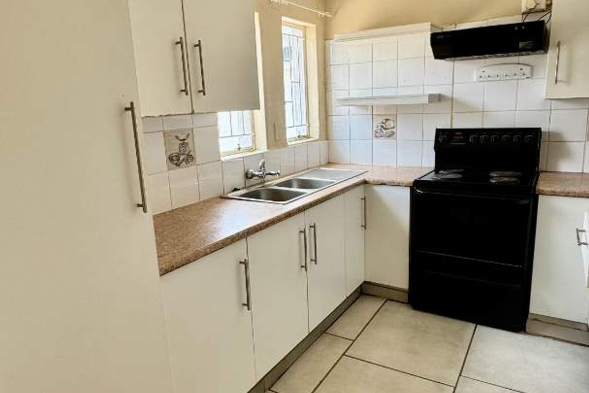 A compact kitchen featuring white cabinetry, laminate countertops, a tiled backsplash, and a freestanding electric stove.