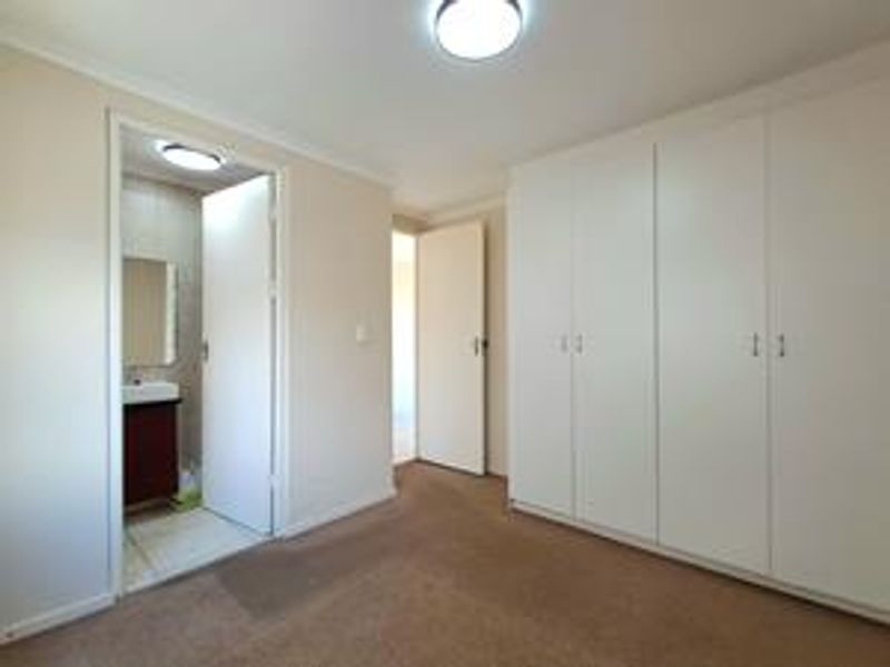 A clean, empty bedroom featuring built-in cupboards, neutral carpeting, and direct access to an en-suite bathroom.