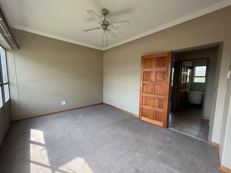 An empty bedroom featuring carpet flooring, a ceiling fan, and a wooden door leading to an en-suite bathroom.