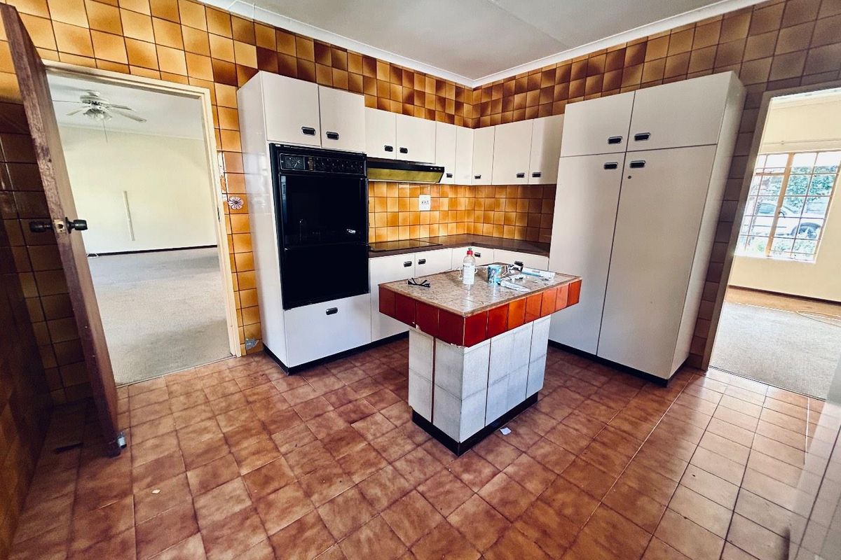 A dated kitchen featuring original brown wall tiles, built-in cabinetry, a central island, and a built-in oven, offering significant potential for modern renovation.