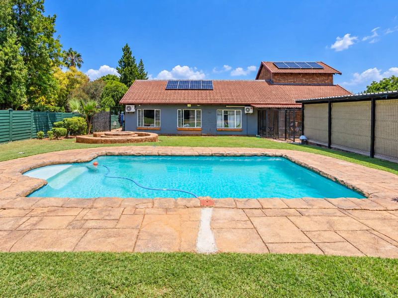 Rear garden featuring a swimming pool with paved surround, a brick fire pit, and a main house structure equipped with solar panels.