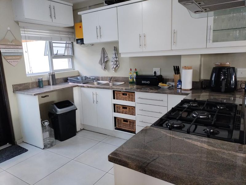 A functional kitchen featuring granite countertops, a gas hob with extractor fan, double sink, and ample built-in cabinetry with tiled flooring.