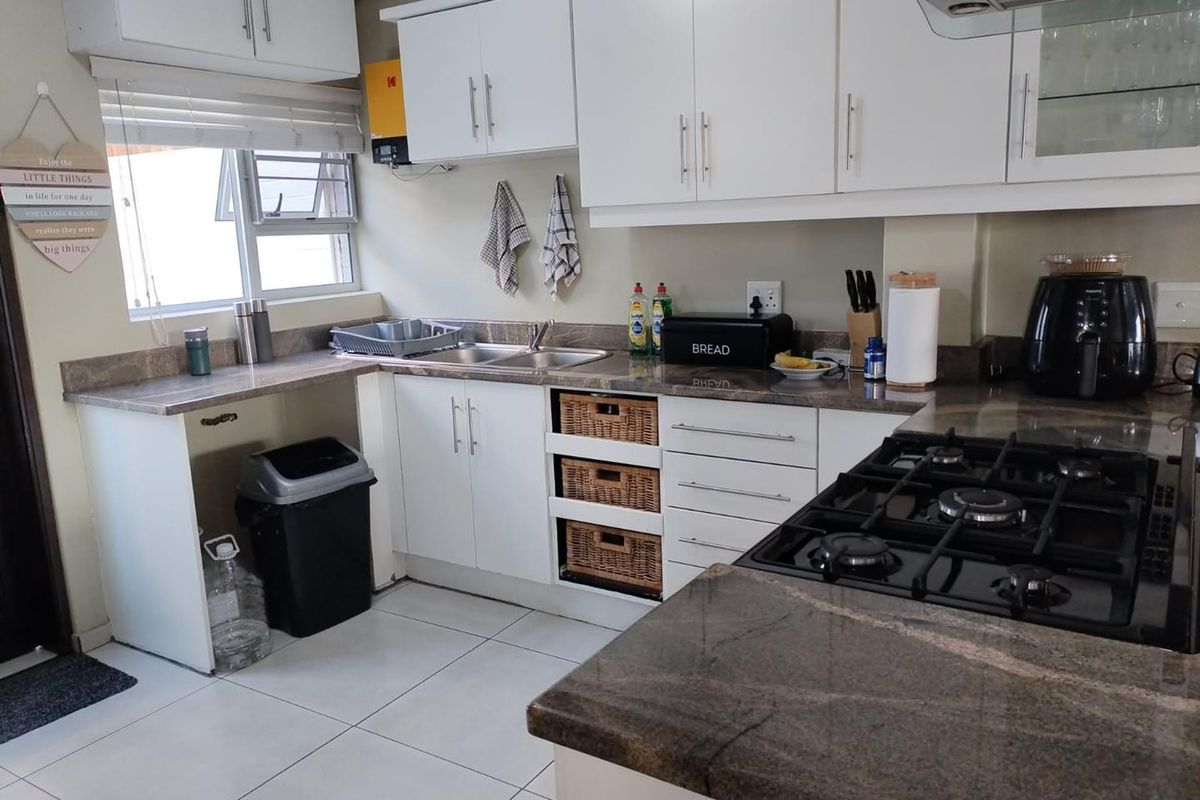 A functional kitchen featuring granite countertops, a gas hob with extractor fan, double sink, and ample built-in cabinetry with tiled flooring.
