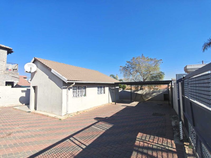 Front exterior view of the property featuring a paved driveway, a covered carport, and secure boundary walls with gated access.