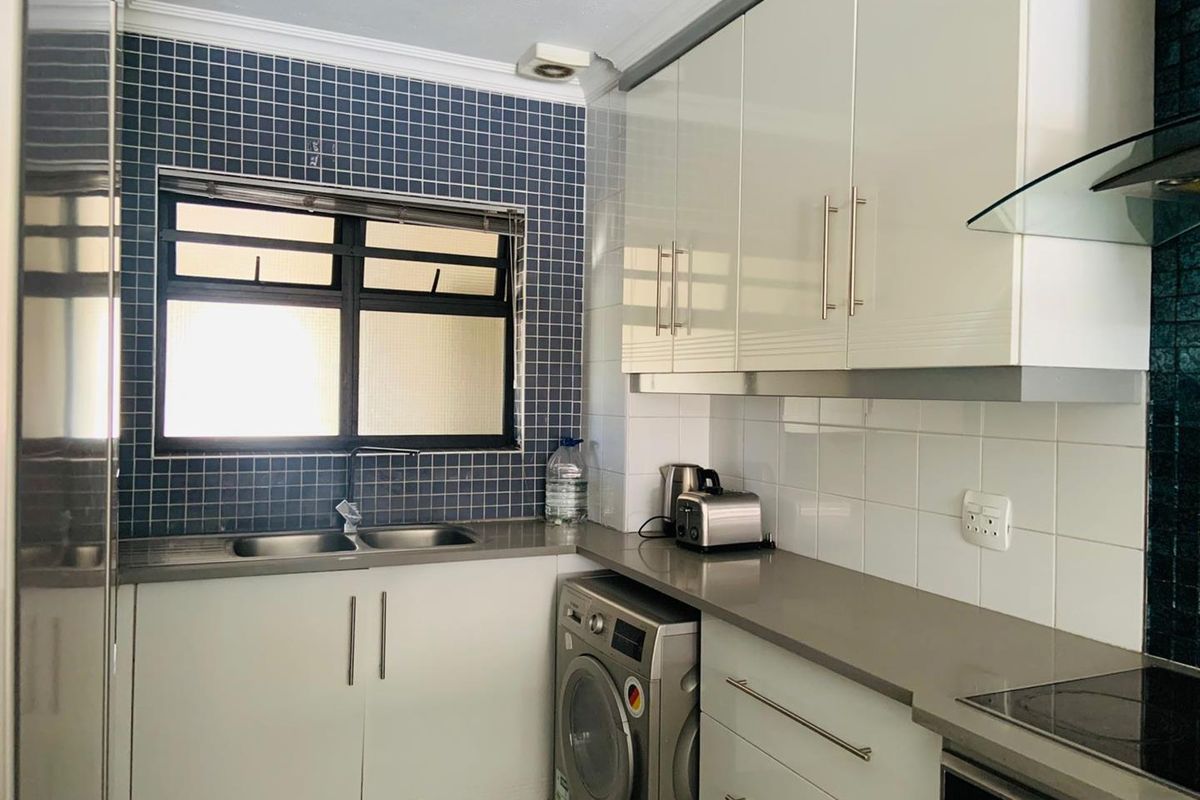 A functional kitchen featuring white cabinetry, stone countertops, a double sink, and a built-in extractor fan with blue mosaic tile backsplash.