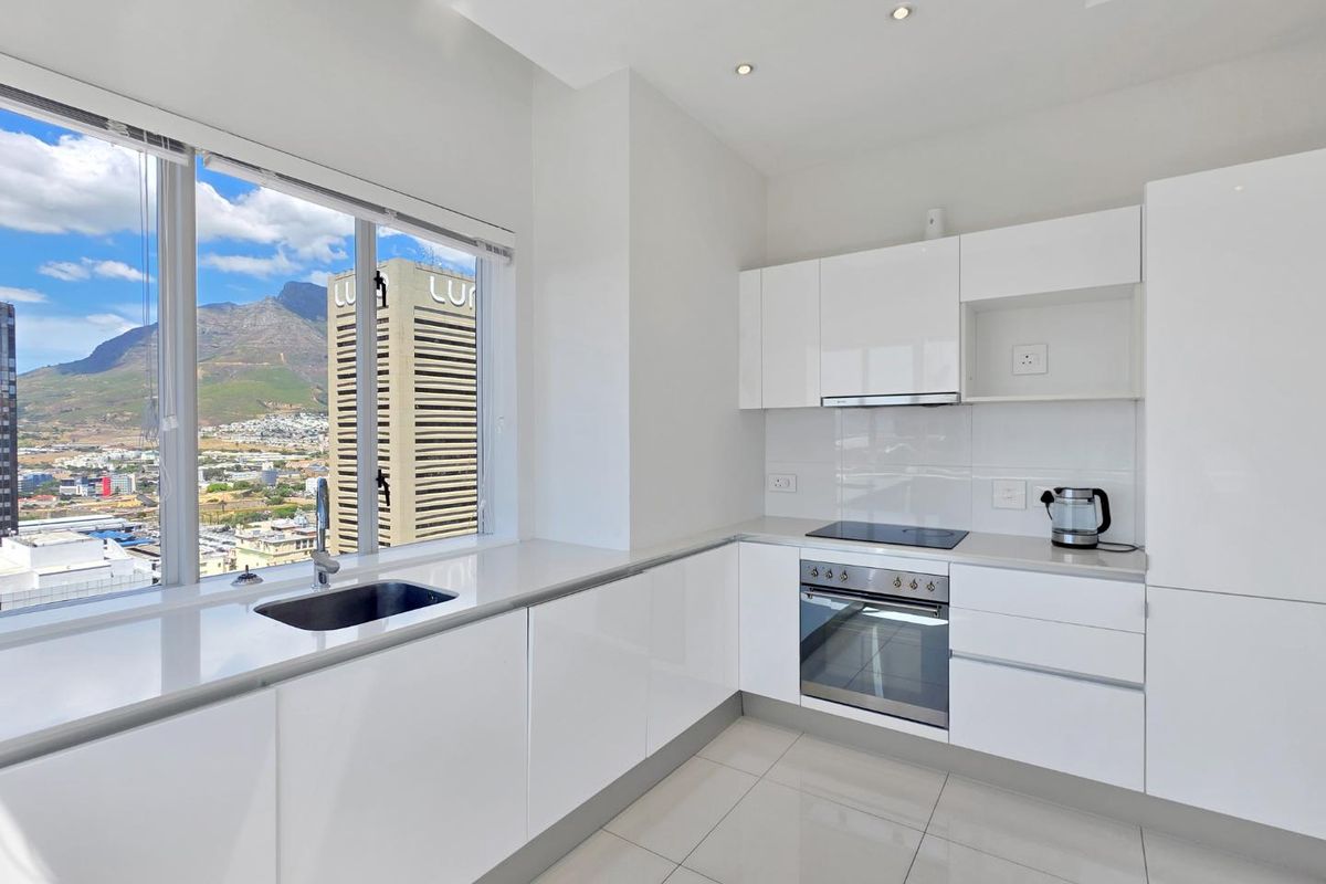 Modern, minimalist kitchen featuring high-gloss white cabinetry, integrated appliances, stone countertops, and large windows offering expansive city and mountain views.