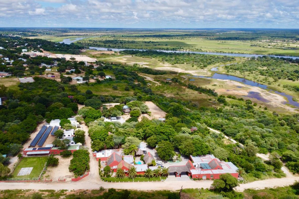 Aerial view of a hotel property featuring multiple buildings with red roofs, solar panel installations, and lush surrounding landscape near a river.