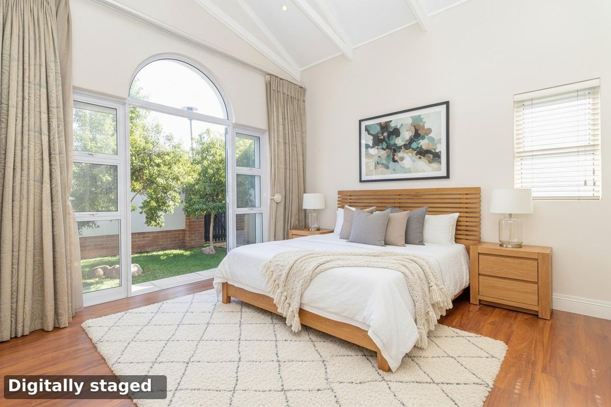 Bright bedroom featuring vaulted ceilings, hardwood flooring, and a large arched glass door providing direct access to the private garden.