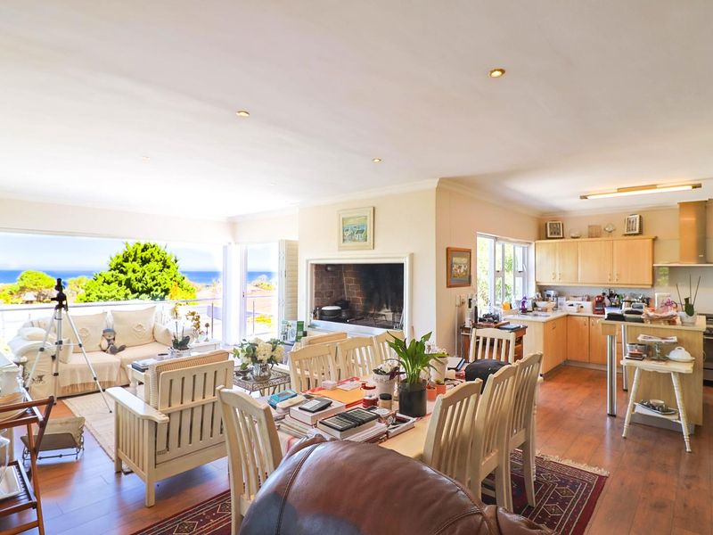Spacious open-plan living, dining, and kitchen area featuring a built-in fireplace, laminate flooring, and large sliding doors opening to a scenic coastal view.