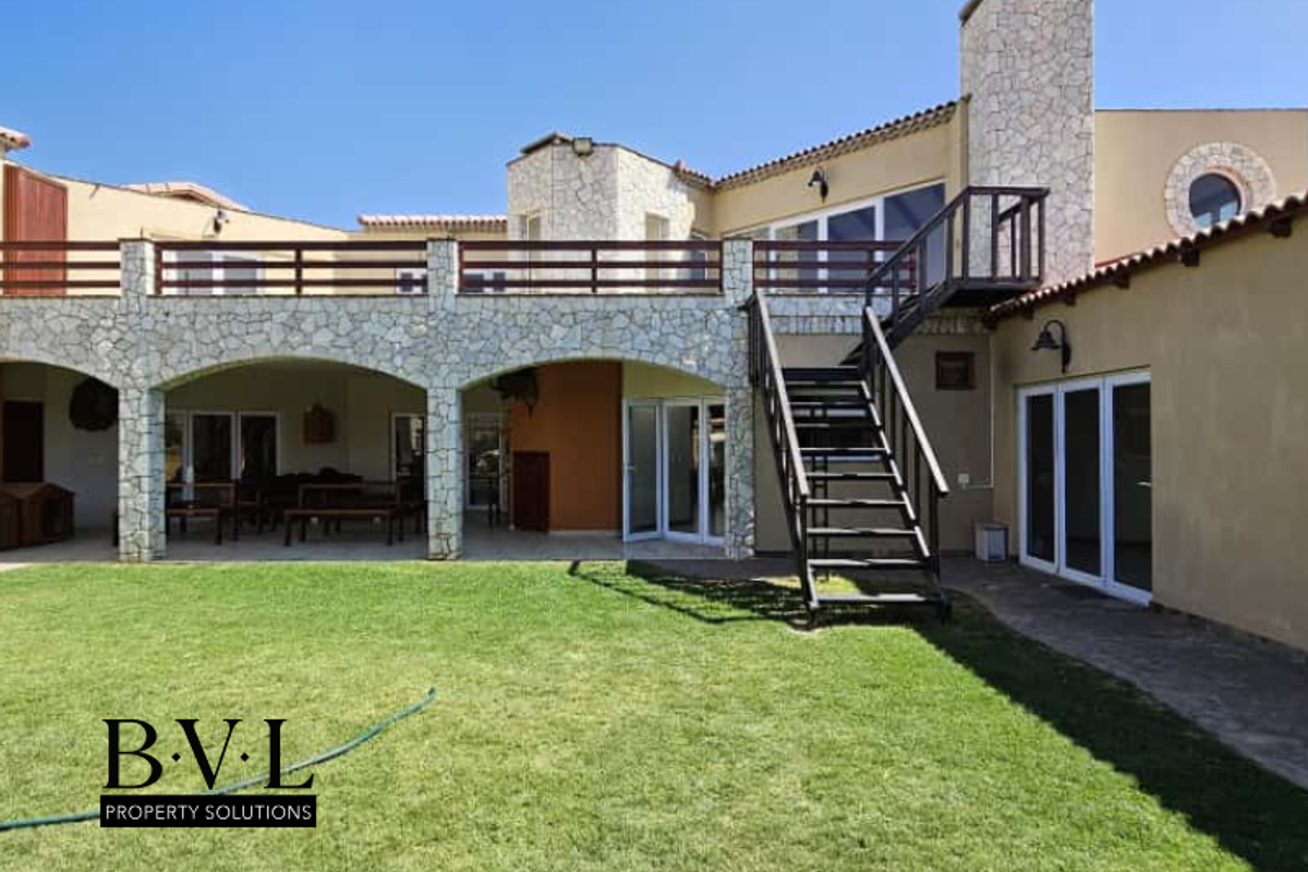 Rear view of the property featuring a stone-clad facade, a spacious covered patio, a large upper-level balcony, and an external metal staircase.