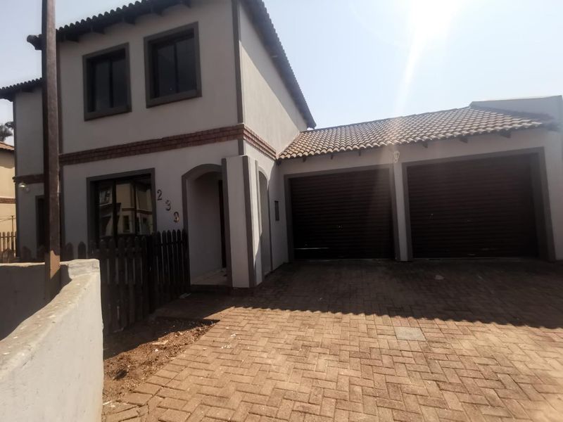 Front elevation of a double-story cluster home featuring a paved driveway, double garage, and a small front garden area with picket fencing.