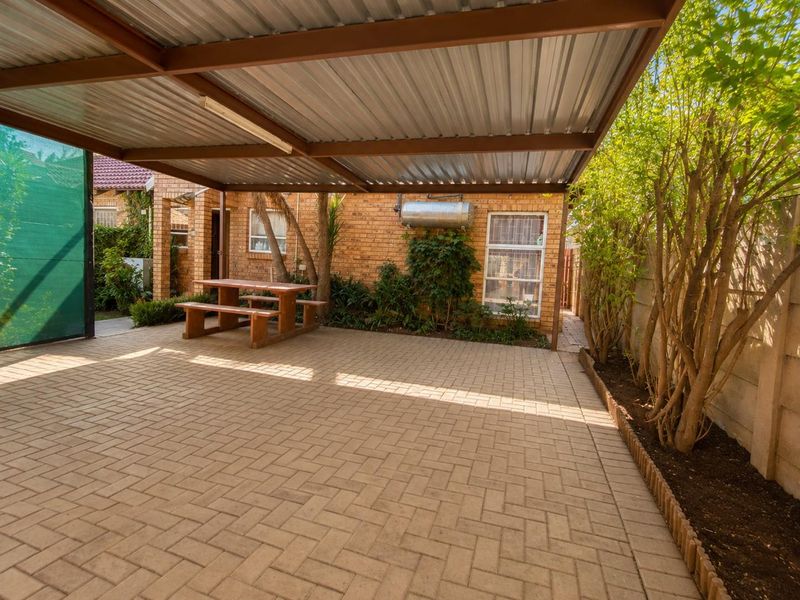 A covered outdoor patio area featuring paved flooring, a corrugated metal roof structure, and direct access to the exterior brick facade of the townhouse.
