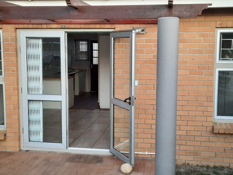 Exterior view of a brick patio featuring a timber pergola, aluminium glass doors, and tiled flooring leading into the home.