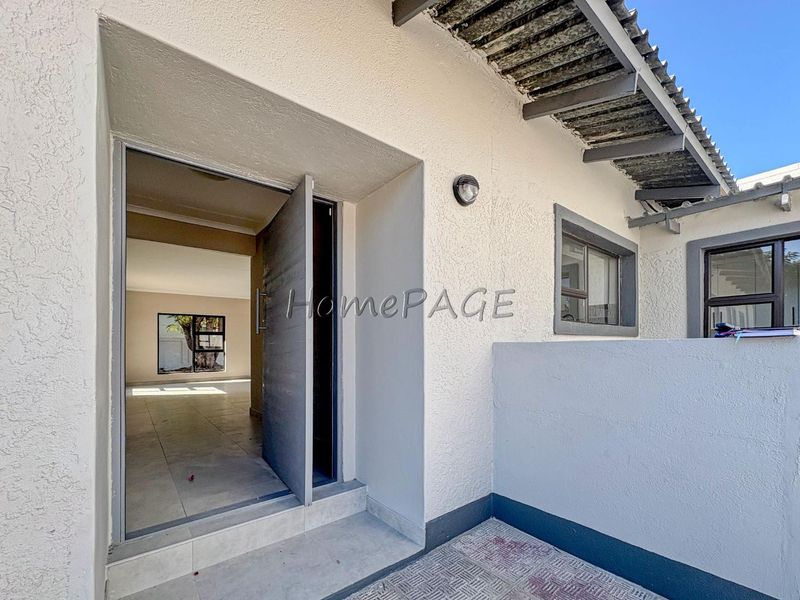 Entrance area featuring a tiled threshold, exterior wall lighting, and an exposed rafter roof overhang leading into the main living space.
