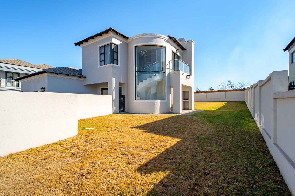 Rear view of the property featuring a spacious garden, a built-in outdoor braai area, and a distinctive curved glass staircase enclosure.