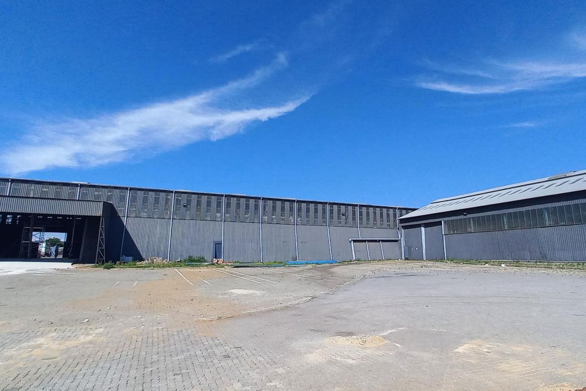 Wide-angle view of an industrial warehouse facility featuring extensive corrugated metal cladding and a large paved yard area.