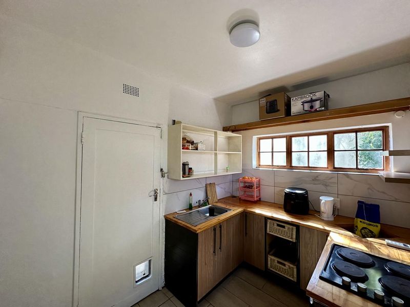 A compact kitchen featuring wooden countertops, a stainless steel sink, built-in hob, and timber-framed windows with tiled backsplash.