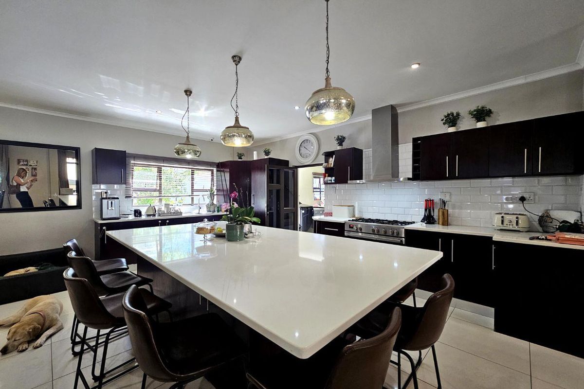 Modern kitchen featuring a large central island with stone countertop, dark cabinetry, subway tile backsplash, and stainless steel gas range with extractor fan.