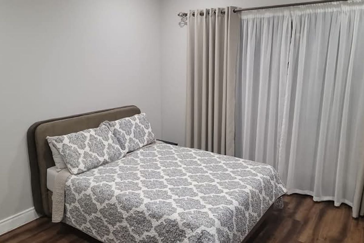 A well-maintained bedroom featuring neutral wall tones, wood-look flooring, and floor-to-ceiling curtains providing natural light control.