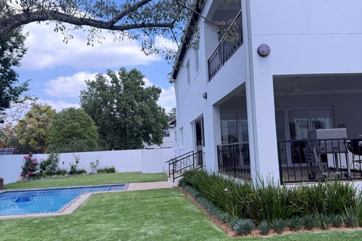 Rear view of the property featuring a swimming pool, landscaped garden, and a multi-level covered patio and balcony with wrought iron railings.