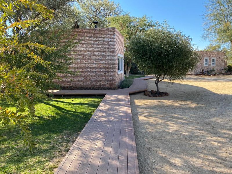 A well-maintained exterior view of a brick farm building featuring a modern timber walkway connecting structures within a landscaped garden setting.