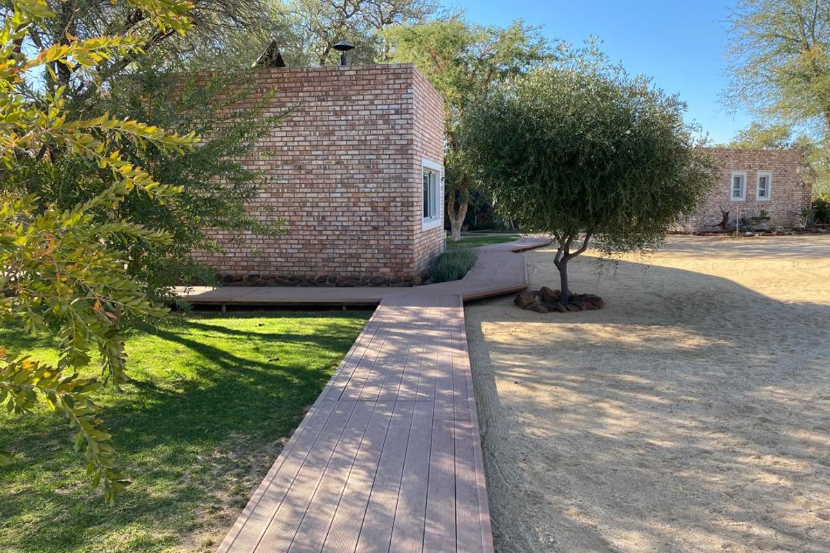 A well-maintained exterior view of a brick farm building featuring a modern timber walkway connecting structures within a landscaped garden setting.