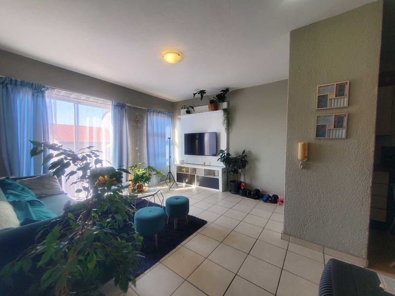 A bright living room featuring tiled flooring, a built-in media unit, and a large sliding glass door providing access to the exterior.