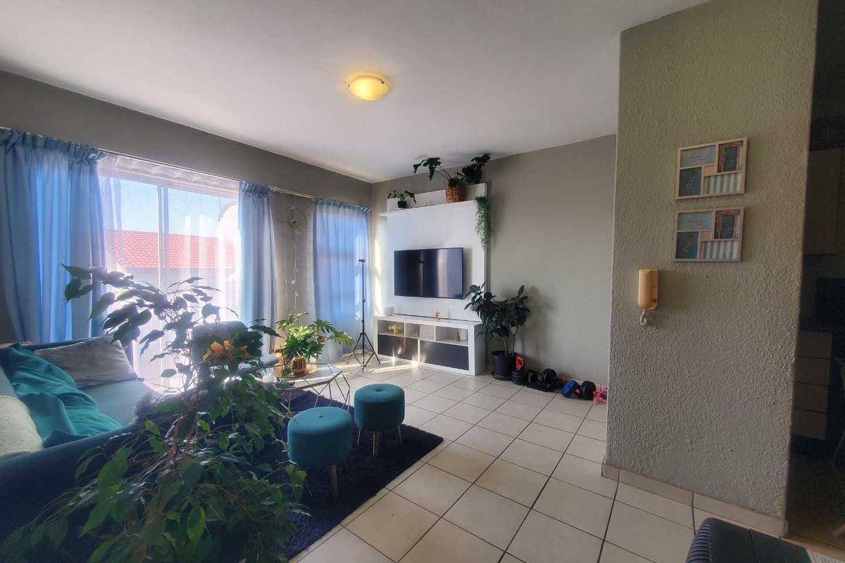 A bright living room featuring tiled flooring, a built-in media unit, and a large sliding glass door providing access to the exterior.