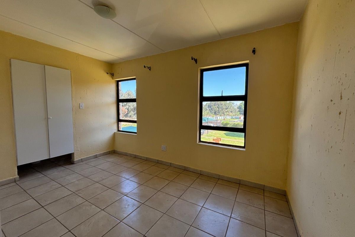 A vacant bedroom featuring tiled flooring, built-in wardrobe, and large windows providing natural light and exterior views.