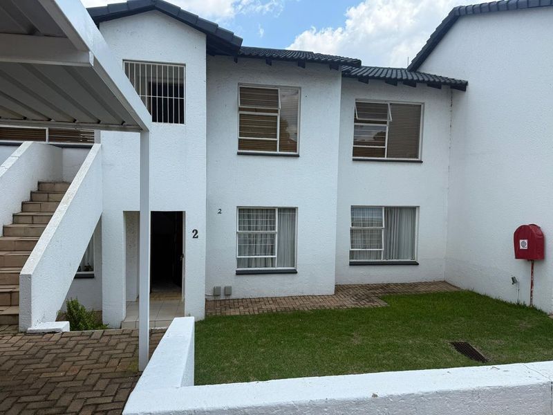 Front elevation of a townhouse unit featuring a paved entrance, small lawn area, and external staircase access.
