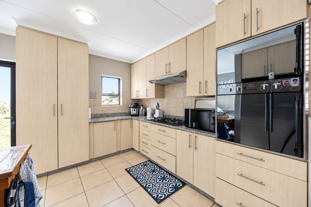 A functional kitchen featuring light wood cabinetry, granite countertops, a gas hob with extractor fan, and a built-in oven, complemented by tiled flooring.