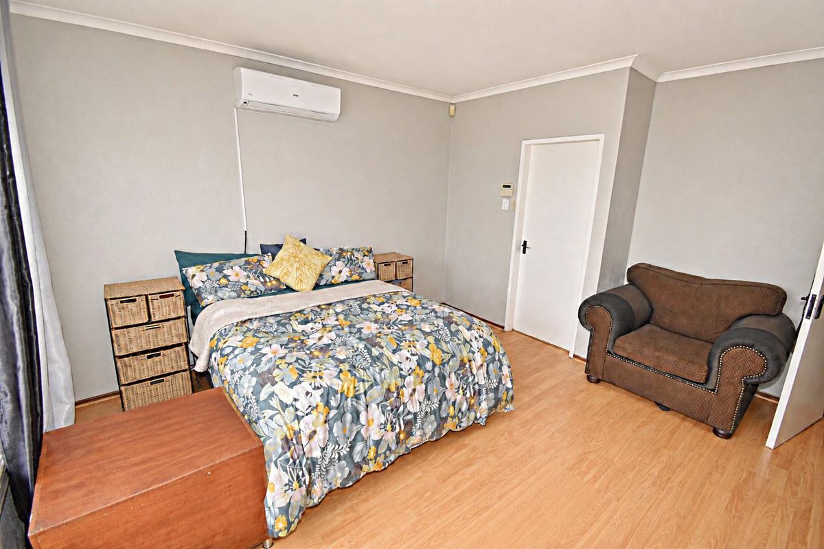 A bedroom featuring laminate flooring, neutral wall paint, and a wall-mounted air conditioning unit.