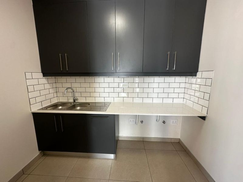A clean, modern laundry area featuring dark cabinetry, a white subway tile backsplash, stone countertops, and a stainless steel sink.