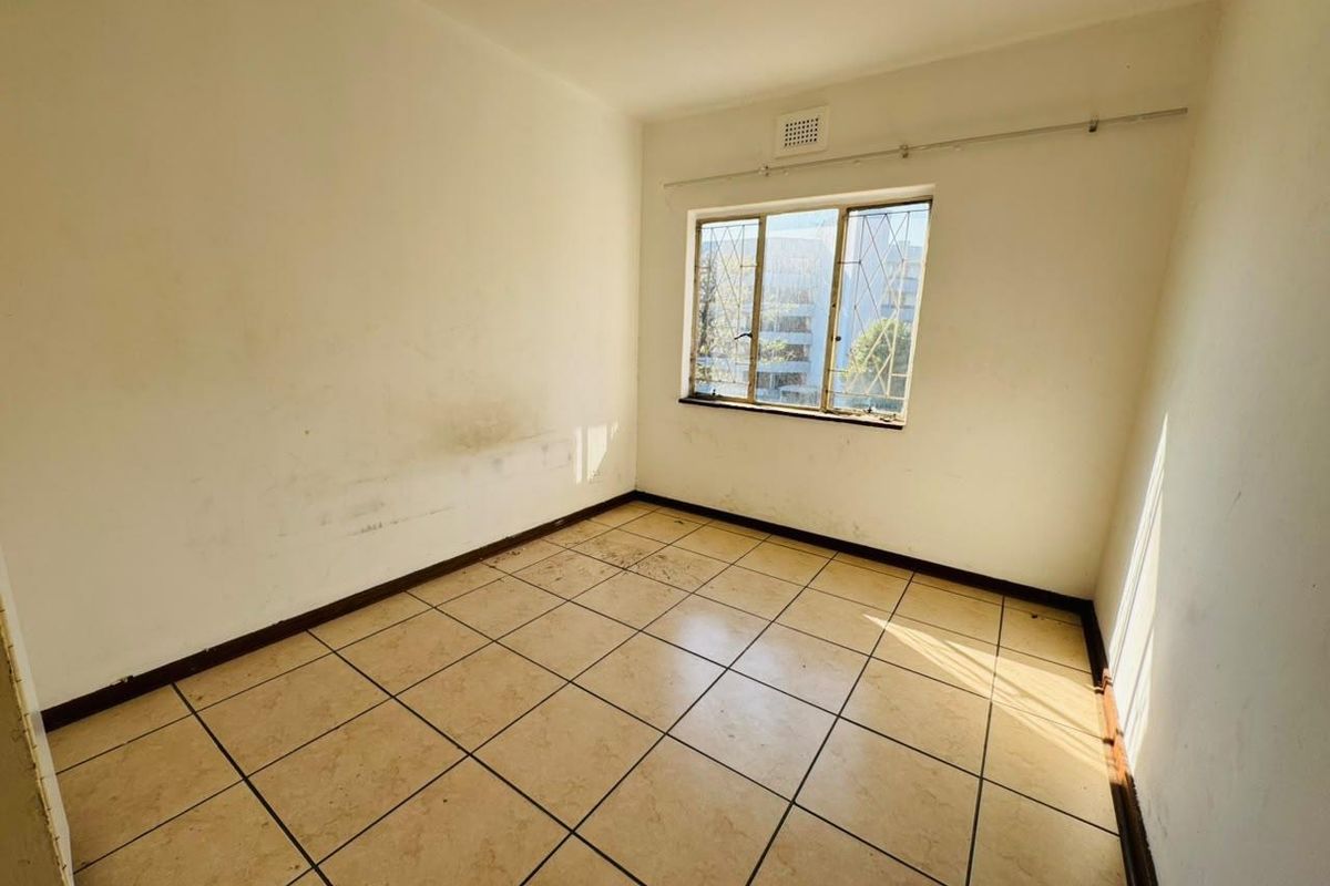 An empty bedroom featuring tiled flooring and a window with security bars, requiring cosmetic updates to the walls and finishes.