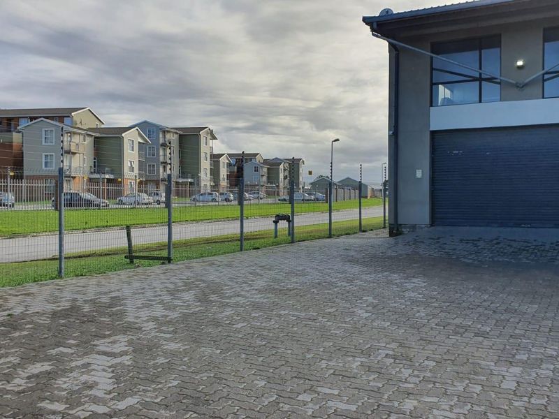Exterior view of a commercial property featuring a paved driveway, roller shutter door, and secure perimeter fencing with electric wires.