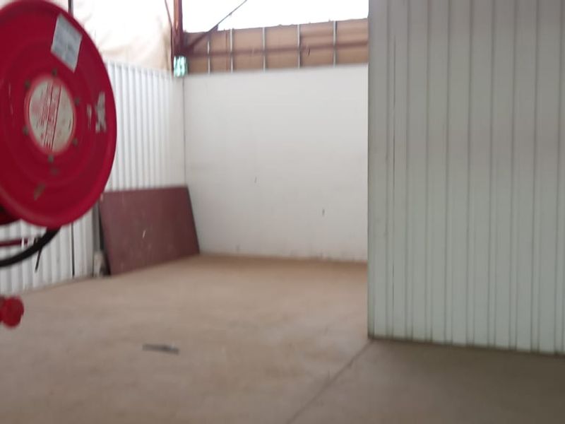 An industrial utility space featuring corrugated metal walls, concrete flooring, exposed steel roof structure, and a mounted fire hose reel.