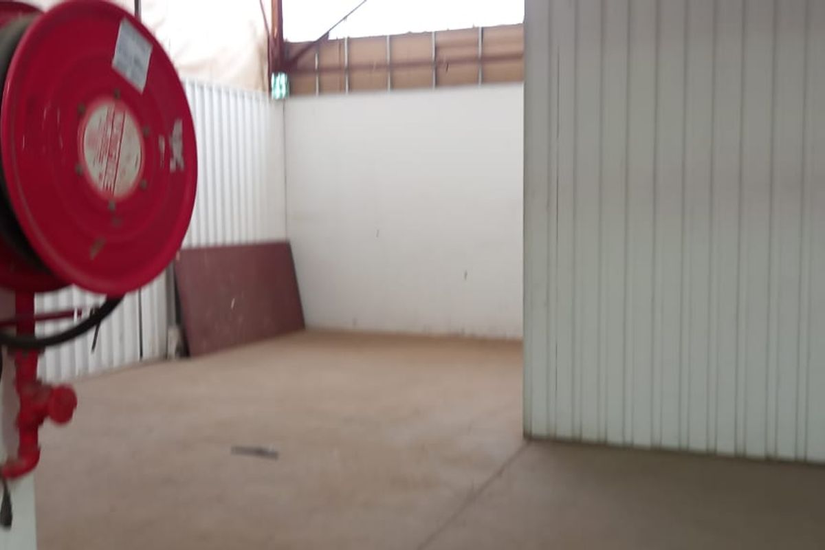 An industrial utility space featuring corrugated metal walls, concrete flooring, exposed steel roof structure, and a mounted fire hose reel.