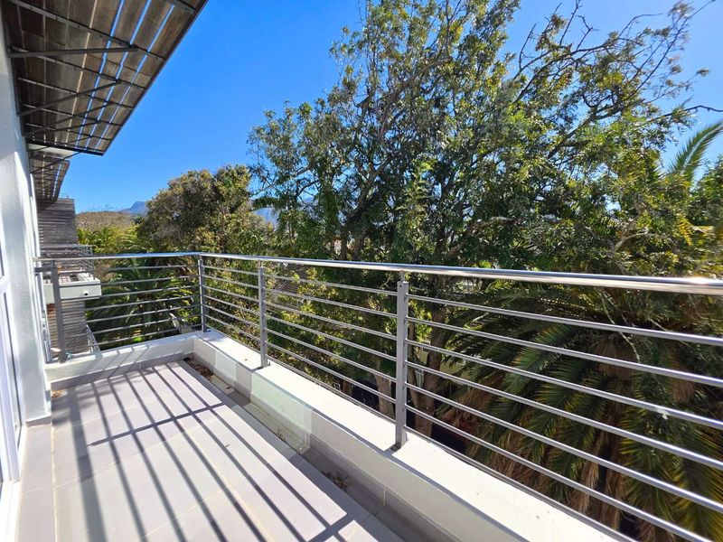 A spacious balcony featuring tiled flooring and a modern stainless steel balustrade, offering a pleasant outlook over surrounding trees.