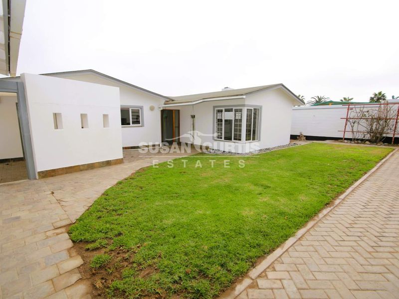 Rear view of the property featuring a paved patio area, a well-maintained lawn, and a bay window.