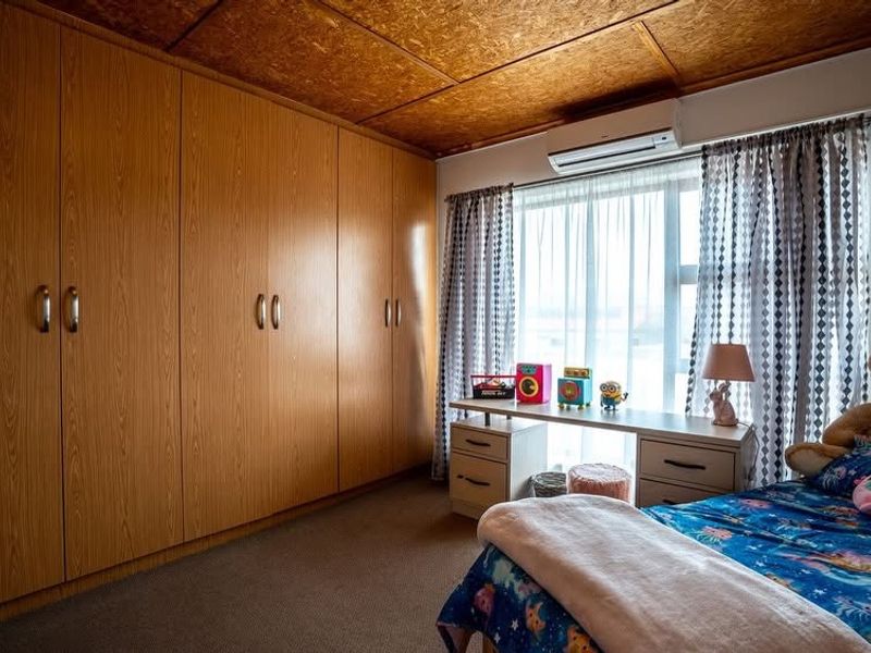 A bedroom featuring extensive built-in timber-look wardrobes, a split-system air conditioner, and a unique timber-paneled ceiling.