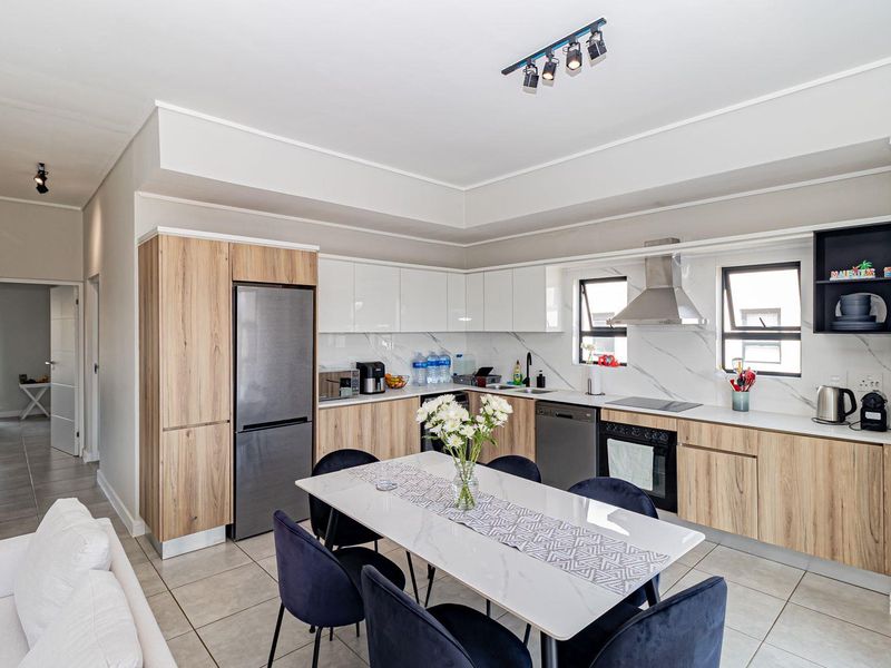 Modern open-plan kitchen featuring wood-grain and white cabinetry, marble-look backsplash, integrated appliances, and sleek tiled flooring in a well-lit penthouse setting.