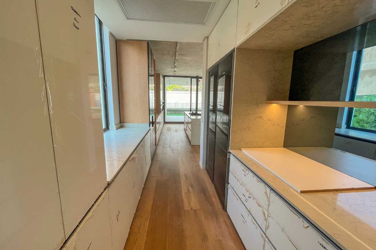 Modern galley-style kitchen featuring high-end cabinetry, stone countertops, integrated appliances, and premium timber flooring with direct access to an outdoor area.