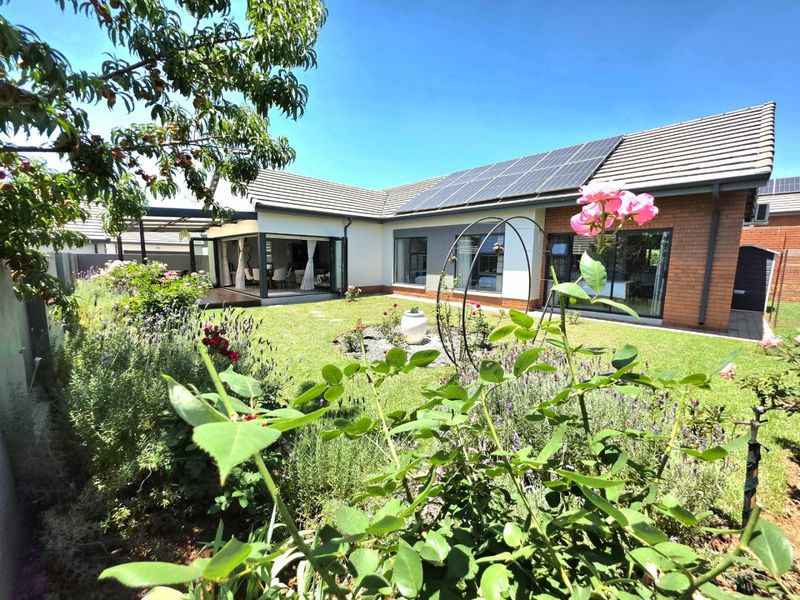 A well-maintained rear garden featuring a landscaped lawn, solar panels on the tiled roof, and seamless indoor-outdoor flow through large sliding glass doors.