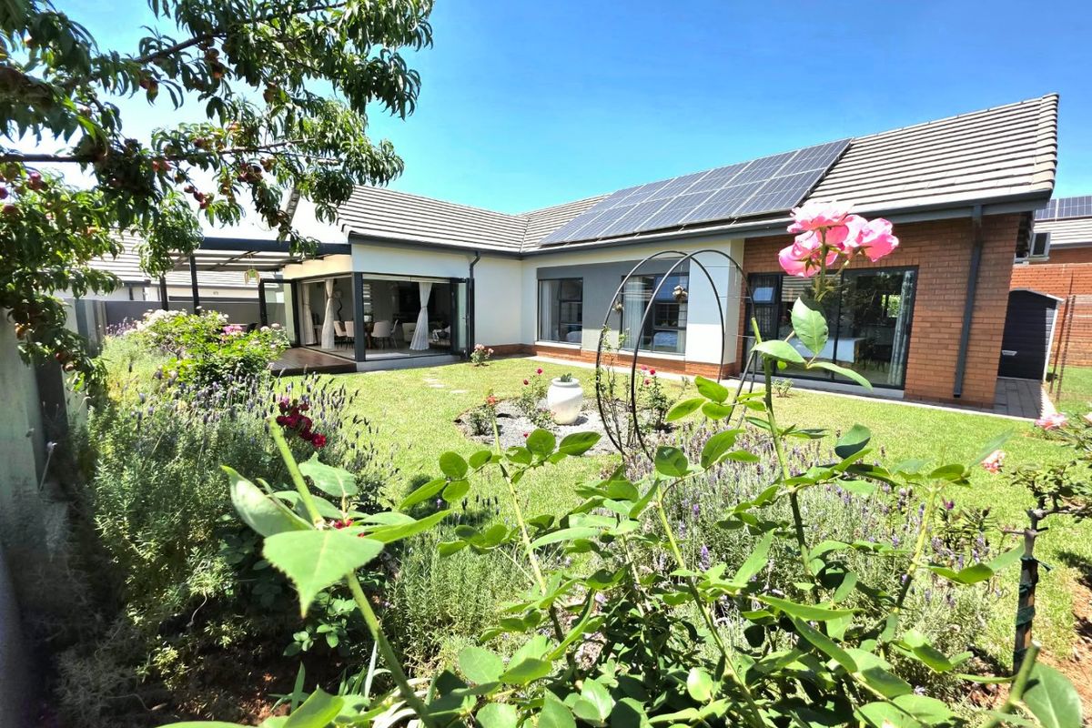 A well-maintained rear garden featuring a landscaped lawn, solar panels on the tiled roof, and seamless indoor-outdoor flow through large sliding glass doors.