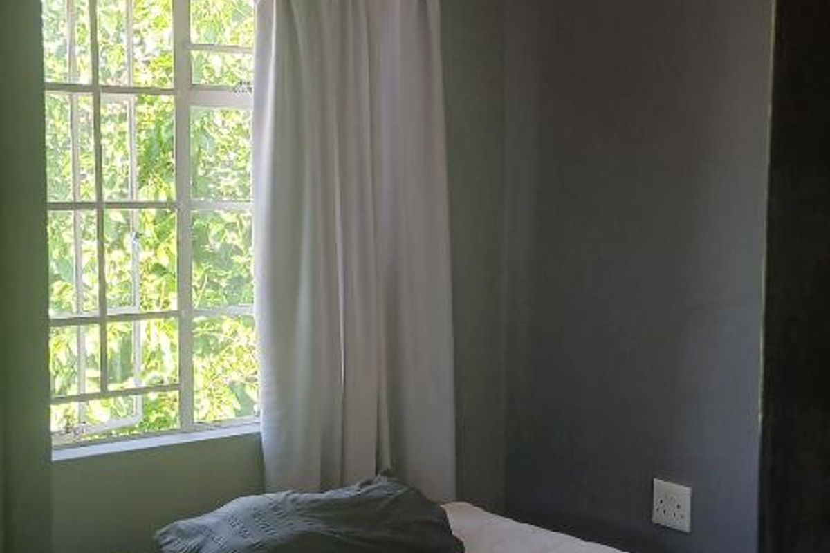 A compact bedroom featuring tiled flooring, a steel-framed window, and neutral wall tones, offering a functional space ready for modernization.