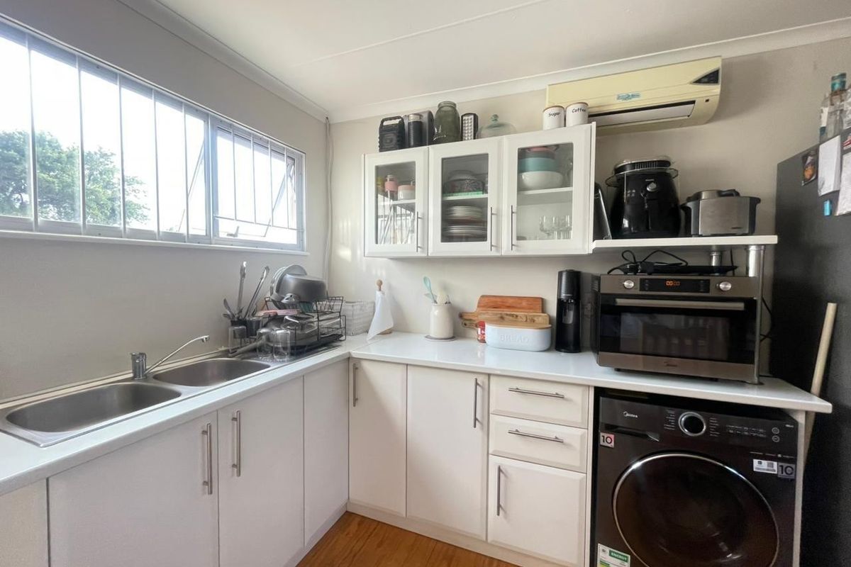 A functional kitchen featuring white cabinetry, laminate countertops, a double bowl sink, and integrated laundry facilities, providing a practical workspace.